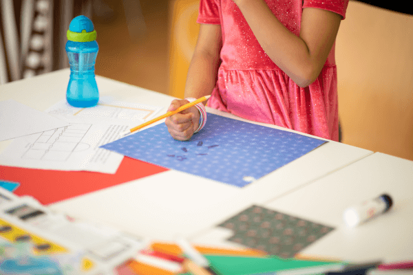 A photograph of a young person drawing on a patterned piece of paper.