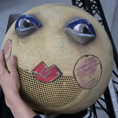 A round circular object with a face drawn on it, including rosy cheeks and red lips.