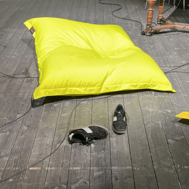 A large yellow bin bag on the floor next to a pair of black trainers.