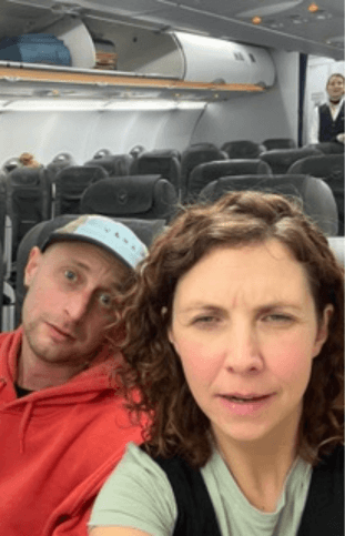 Two people sat side by side on an aeroplane taking a selfie.