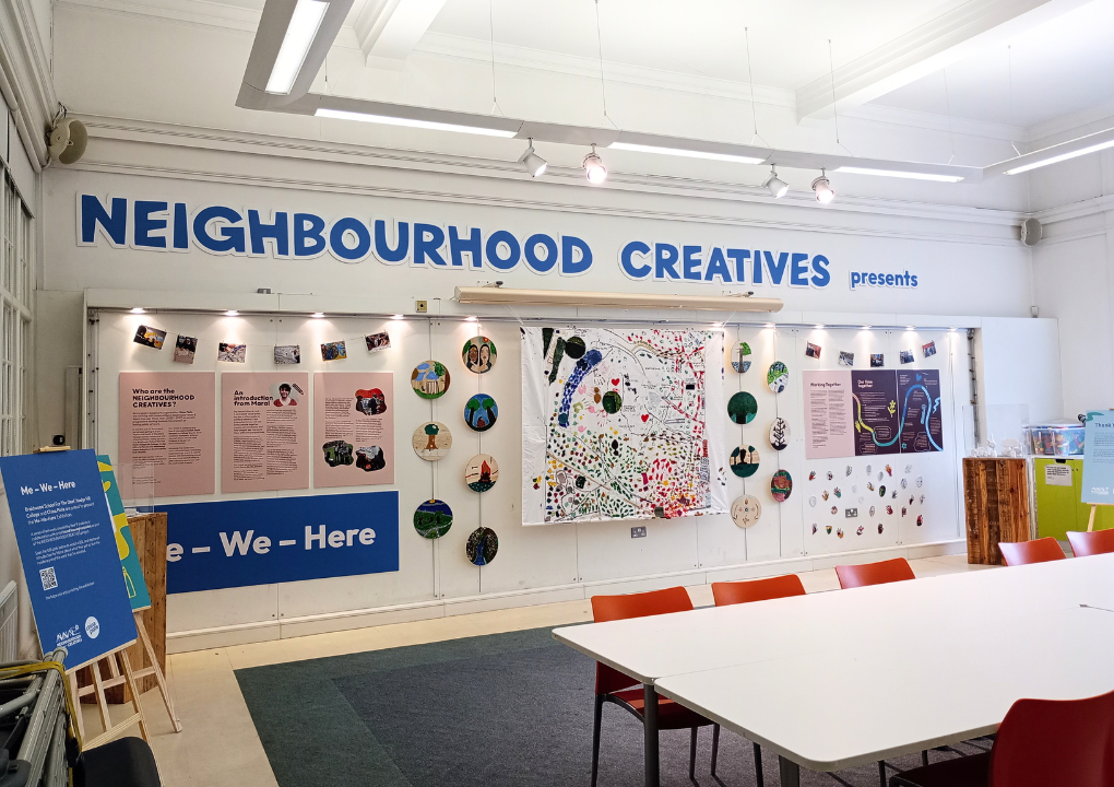A wide angle view of the Me We Here exhibition at Ward End Library including information display boards, hanging circular wooden paintings and clay sculptures and a large fabric map.