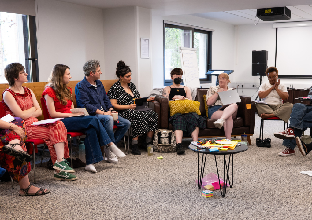 Seven people sat round in a circle, listening to one person who is speaking to the room.