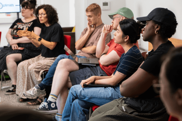 A group of people sitting in a circle, listening to someone out of shot.